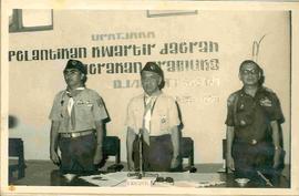 Sri Sultan Hamengku Buwono IX berbaju pramuka berdiri diantara Moenadi dan seorang TNI mengikuti ...