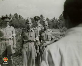 Dua orang gerilyawan TNI berdiri tegap di samping tentara asing membelakangi areal persawahan.