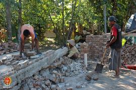 3 (tiga) orang warga sedang membersihkan puing- puing bangunan rumah yang roboh dengan mengumpulk...