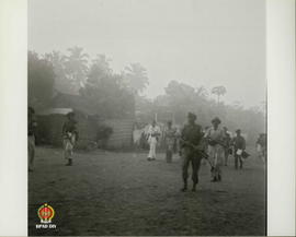 Rombongan gerilyawan bersenjata senapan berjalan dengan siaga di samping perkampungan  penduduk.