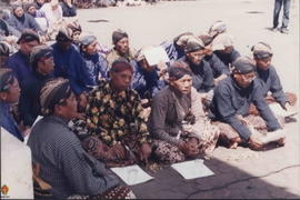 Tampak Bapak-bapak dengan pakaian adat Jawa duduk bersila di tengah terik matahari guna mendukung...