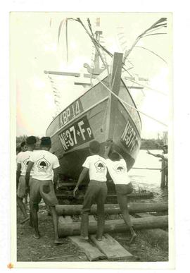 Beberapa orang memakai kaos Golkar menurunkan perahu ke laut dengan menggunakan balak kayu dalam ...