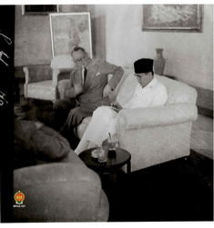 Presiden Soekarno sedang berbicara dengan Stikker sambil menulis dalam buku catatan di Istana Neg...