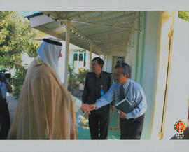 Seorang laki- laki berjabat tangan dengan perwakilan dari Bulan Sabit Kuwait untuk menyambut keda...