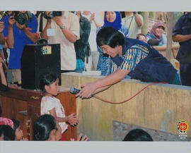 Kak Seto Mulyadi sedang menyodorkan microphone kepada anak yang sedang bernyanyi.