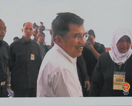 Wakil Presiden RI Yusuf Kalla sedang tertawa dan di belakangannya rombongan tamu wakil kepresidenan.