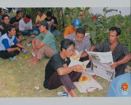 Situasi para korban gempa bumi sedang istirahat sambil makan dan ada yang membaca surat kabar.