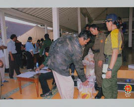 Seorang korban gempa bumi yang menerima beras dan di saksikan anggota linmas.